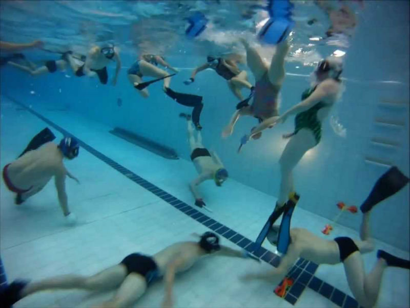 A full team of underwater hockey players swimming at different depths during a game